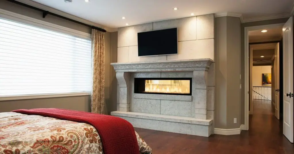  Elegant bedroom featuring stone fireplace and mounted TV